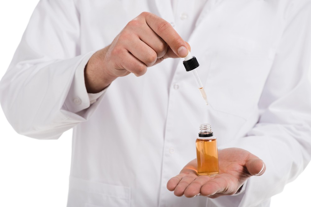 Doctor in lab coat dispensing amber CBD oil from dropper into bottle, quality tinctures available at premier CBD store Broken Arrow for health and wellness.