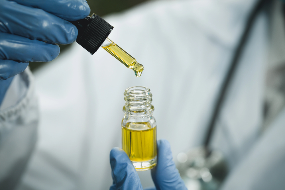 Medical professional holding out golden CBD tincture bottle with dropper, trusted products from leading CBD store Broken Arrow for natural remedies.