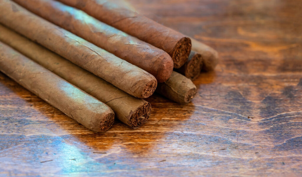 Close up of premium hand-rolled tobacco cigars stacked on a rustic wood table at a professional cigar shop Owasso.