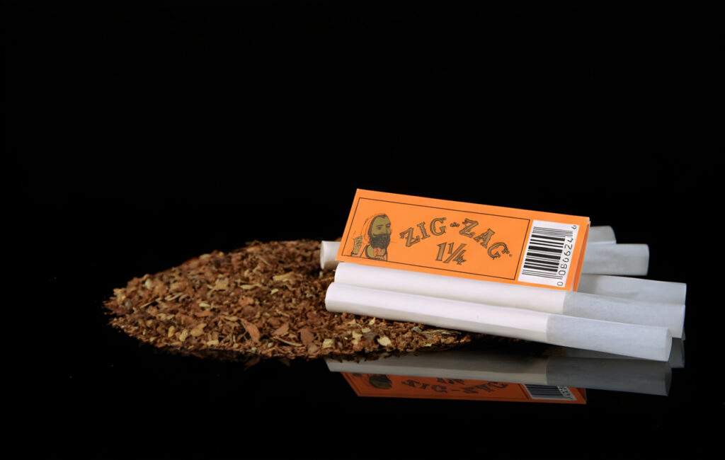Classic orange Zig-Zag rolling papers Houston smokers prefer, stacked with rolled cigarettes on a black surface.