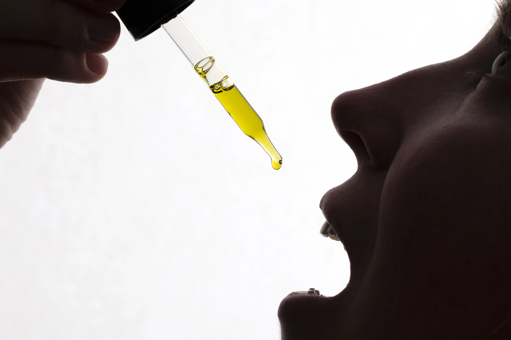Silhouette of person administering CBD oil drop under tongue for quick absorption, effective tinctures from leading CBD store Broken Arrow.