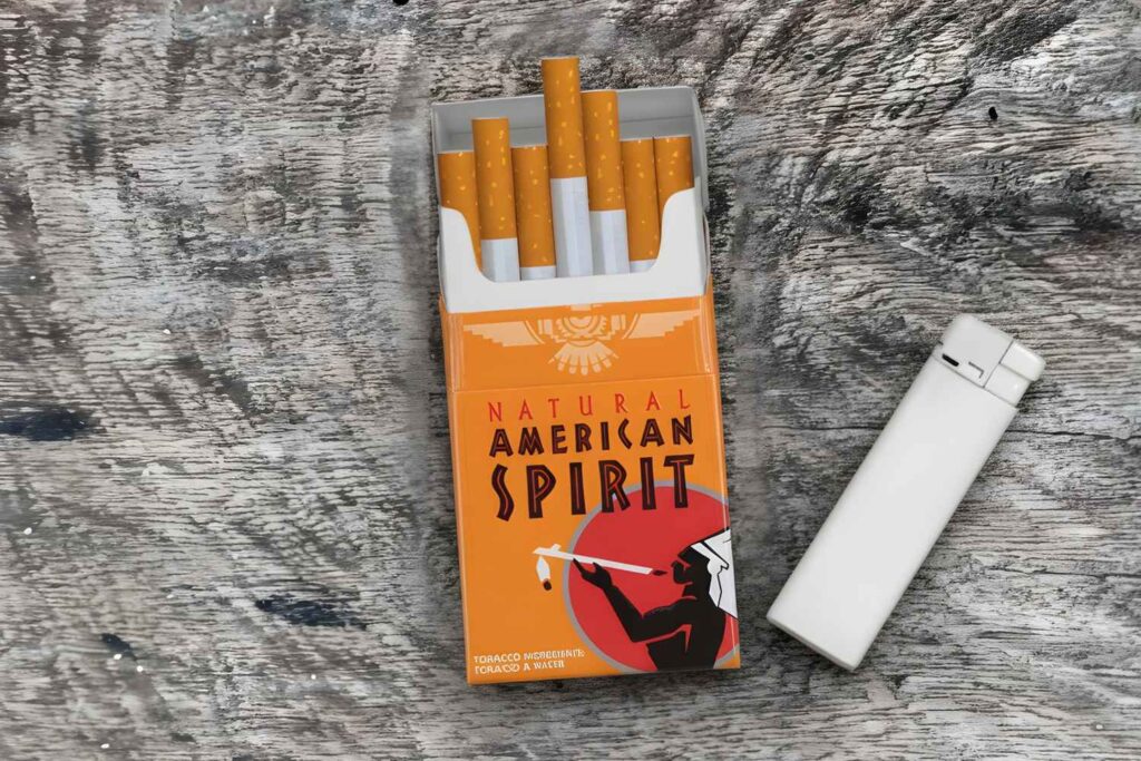 American Spirit Orange pack and lighter on wood at a tobacco store Houston featuring additive free filter cigarettes.