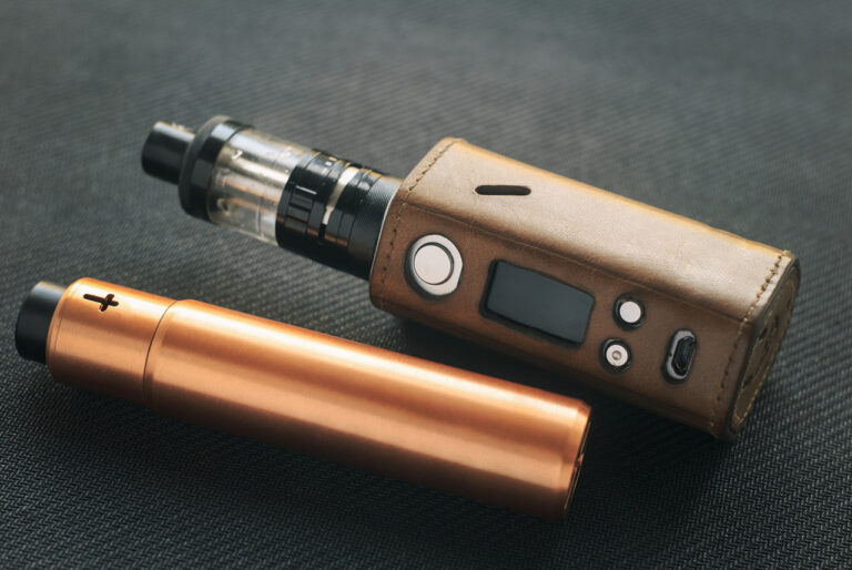 Vape shop Houston advanced setup: a box mod with a leather case next to a copper-colored mechanical mod device.