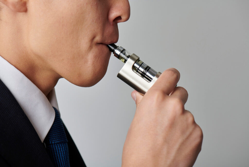 Professional businessman in a suit using a sleek silver vape mod; available at our top-rated vape shop Houston.