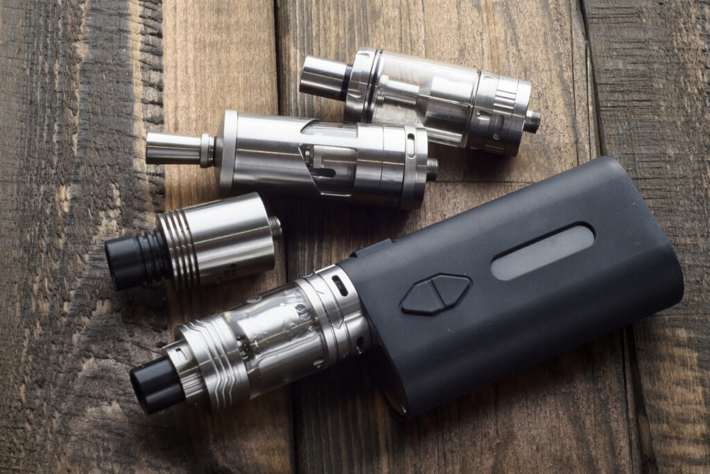 Vape shop Houston display of modular tank and mod parts on a wooden table, showing different coil and glass sections.