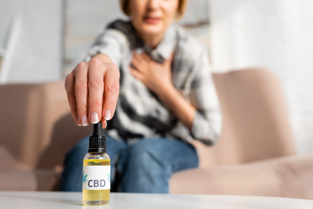 Woman reaching for premium CBD oil tincture on table for natural relief, available at top CBD store Broken Arrow with quality wellness products.