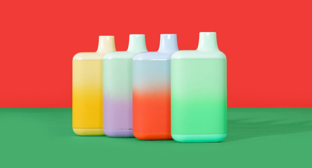 Four colorful gradient disposable vaporizers lined up against a red background, available at your local vape shop Tulsa.