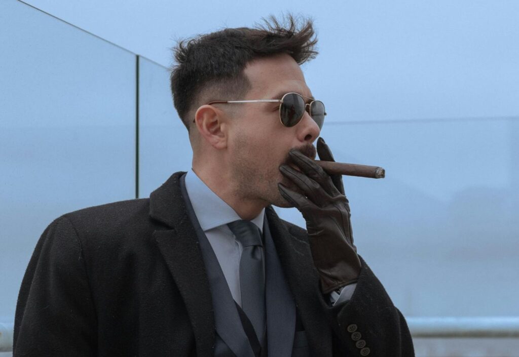 Well-dressed man in a coat and sunglasses smoking a hand-rolled cigar from a premier cigar shop Houston boutique.
