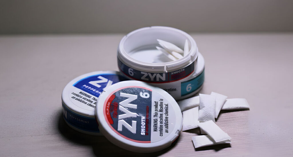 Open Zyn Smooth nicotine pouch cans and white pouches on a counter, sold at our local tobacco shop Houston store.