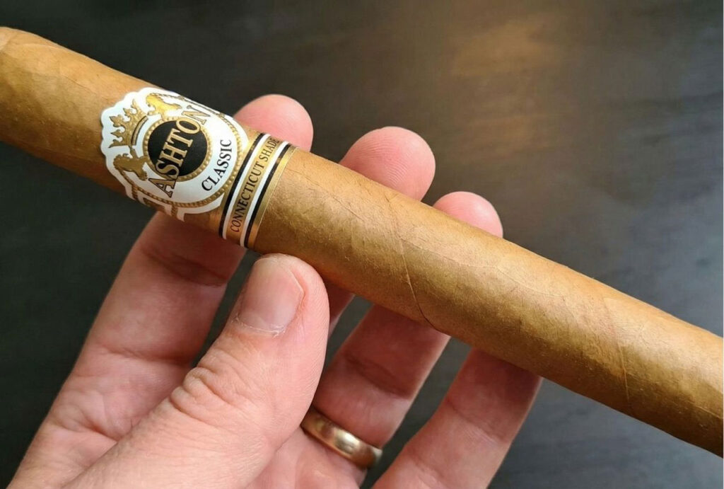 Close-up of a hand holding an Ashton Classic cigar. Shop for premium brands at a local cigar store broken arrow.
