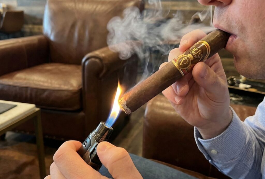 A man in a lounge lights an Oliva Serie V cigar with a torch lighter while taking a draw, a common practice for patrons of a cigar shop sapulpa.