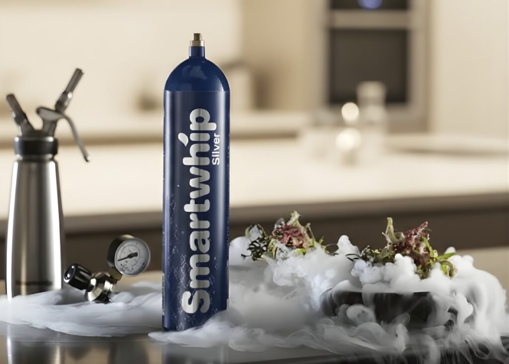 Silver Smartwhip nitrous oxide Owasso cylinder on a kitchen counter with a pressure gauge and infusion fog. 