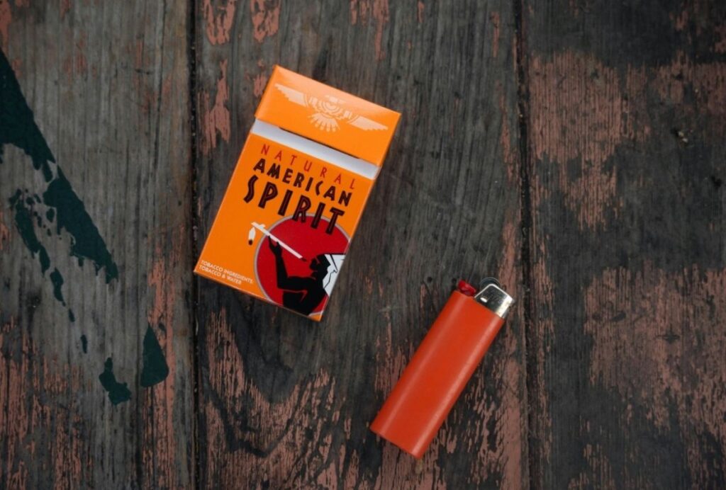 Top view of an orange Natural American Spirit pack and lighter on rustic wood, ideal for a cigarette shop Sapulpa blog post.