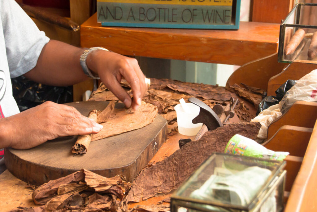 Focused hands of an artisan rolling a premium cigar on a wooden block. Find your next quality smoke at our premier cigar shop Sapulpa.