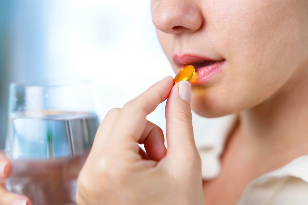 A woman taking a gold gel capsule with water from a glass, highlighting products from a delta 8 store broken arrow.