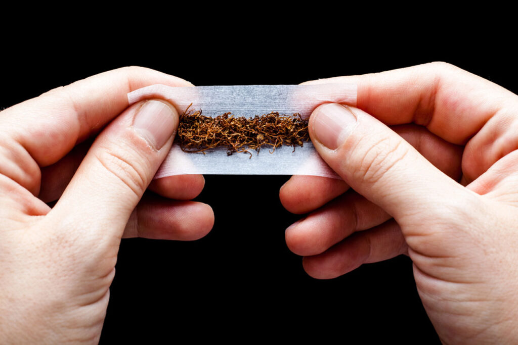 Close-up of a person rolling loose-leaf tobacco into white rolling papers. This is a crucial step for rolling papers houston enthusiasts.