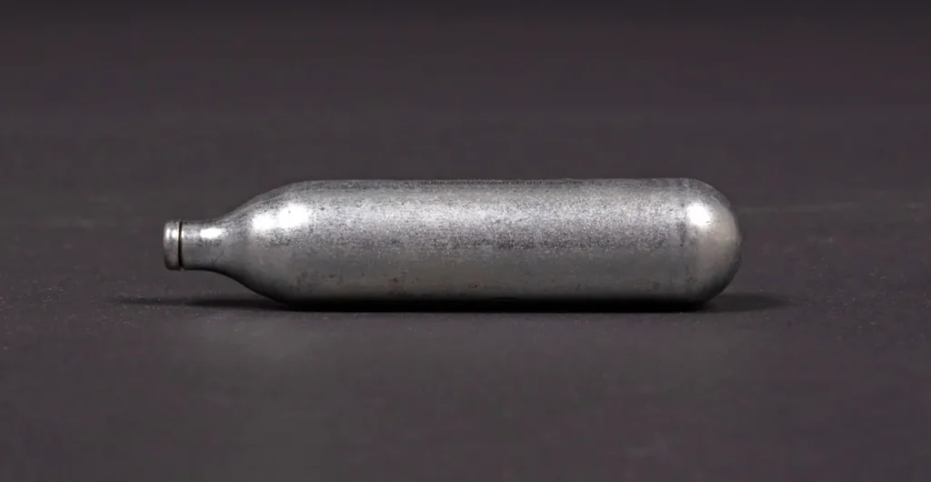 A close-up of a single 8g silver N2O cylinder on a dark background. We sell premium whip cream chargers owasso.