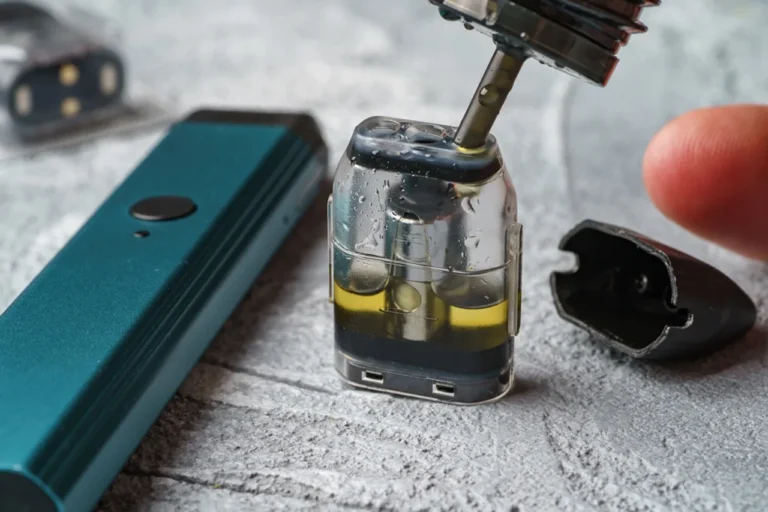 Extreme close-up of an e-liquid bottle tip refilling a clear vape pod, showcasing how refillable nicotine pods Tulsa work.