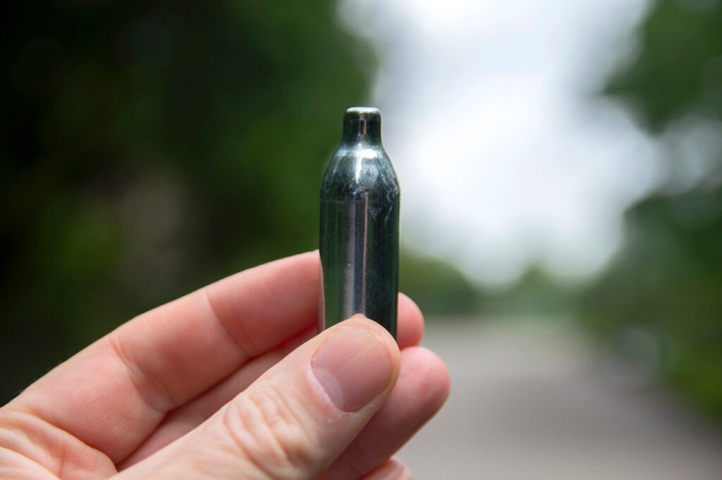 A hand carefully holds one of our nitrous oxide chargers Tulsa against a blurry outdoor background.