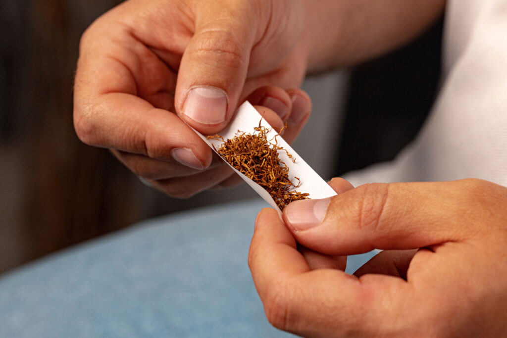Hands carefully rolling tobacco into a white rolling paper, showcasing the texture. Learn the art of rolling papers houston smokers master.