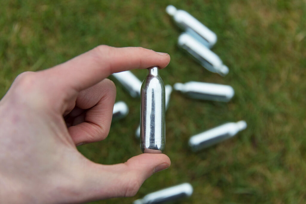 overhead view of a hand holding a charger over multiple scattered nitrous oxide chargers Tulsa on the grass.