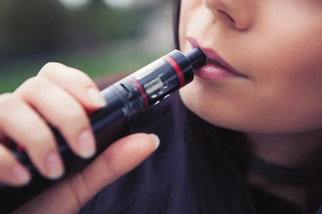 A person taking a puff from a black mod vape. Explore our guide on the best e-cigarettes broken arrow has to offer.