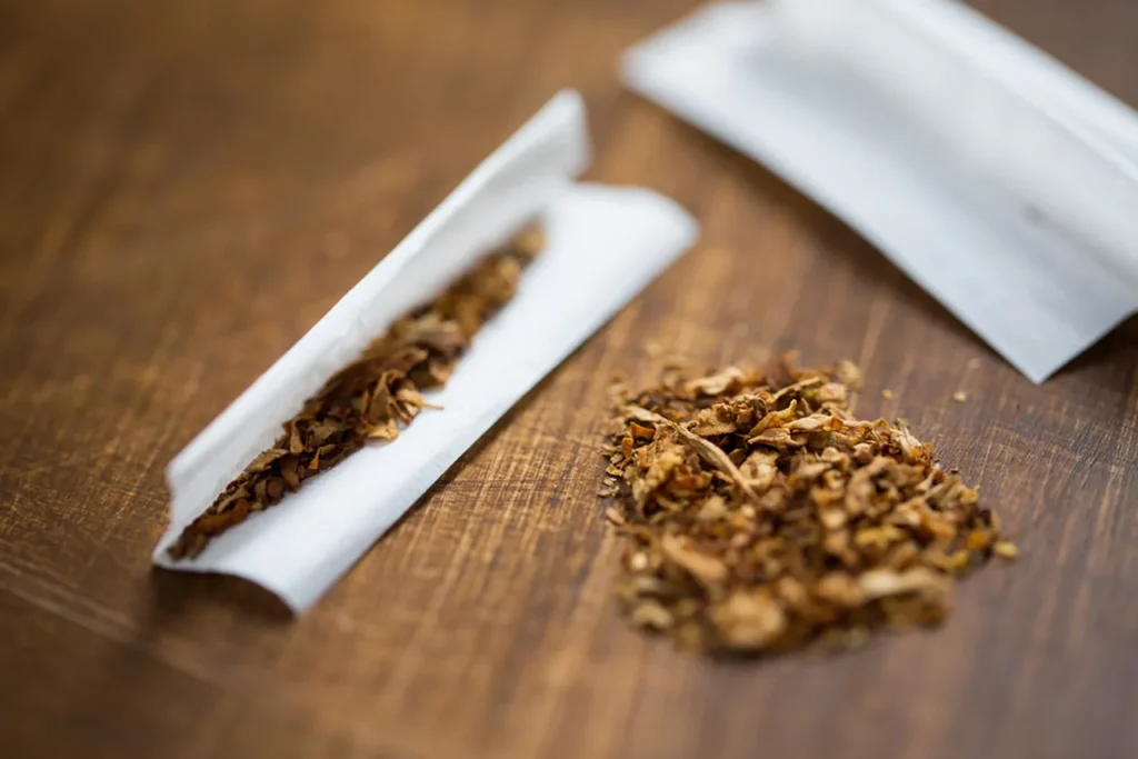 A detailed close-up of loose, shredded tobacco being rolled into high-quality Rolling papers tulsa on a rustic wooden table.