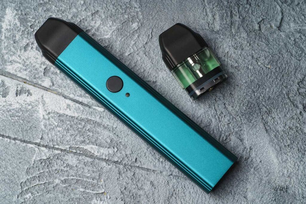 A sleek teal stick vape device and a single clear replacement pod on a grey stone texture, available for nicotine pods Tulsa buyers.