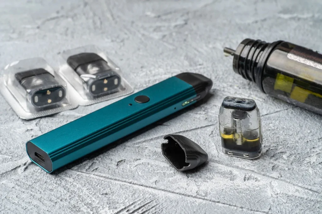 A detailed look at a sleek teal vape device alongside a selection of multi-packs of replacement nicotine pods Tulsa users can buy.