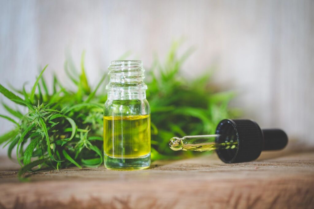 Glass tincture bottle with a dropper and fresh hemp leaves on a rustic bench from a cbd store broken arrow ok.