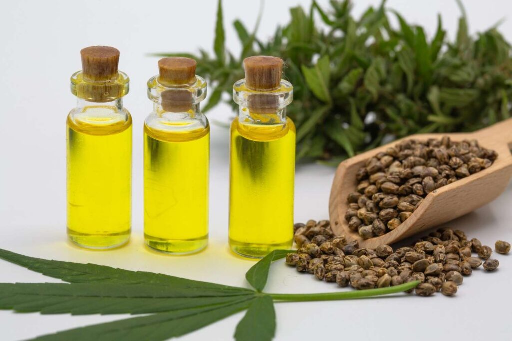 Three clear amber extract bottles next to a wooden scoop of hemp seeds from a local CBD store Broken Arrow.