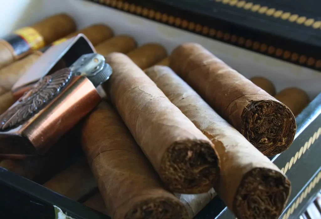 A metal torch lighter resting on top of fresh cigars inside a wooden humidor box at a local cigar shop in Owasso.