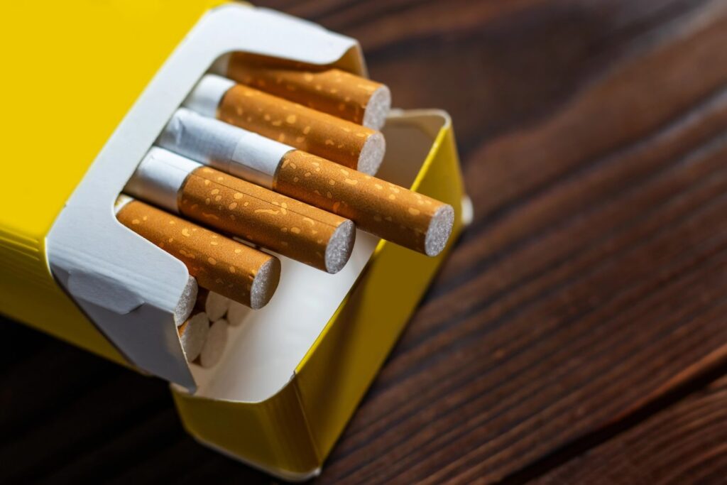 A yellow pack of filtered cigarettes on a dark wood table, available at a local cigarette shop broken arrow retailer.
