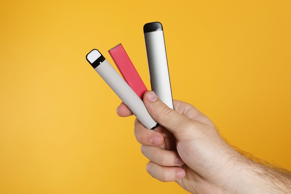 Close-up of a hand holding three sleek, portable nicotine pods tulsa devices in various colors on a yellow background.
