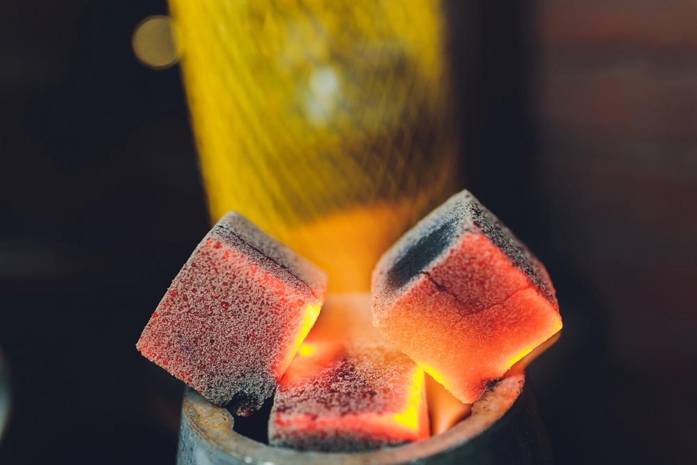 Close-up view of premium, glowing red hookah charcoal cubes burning on a metal electric heater at our hookah shop houston.