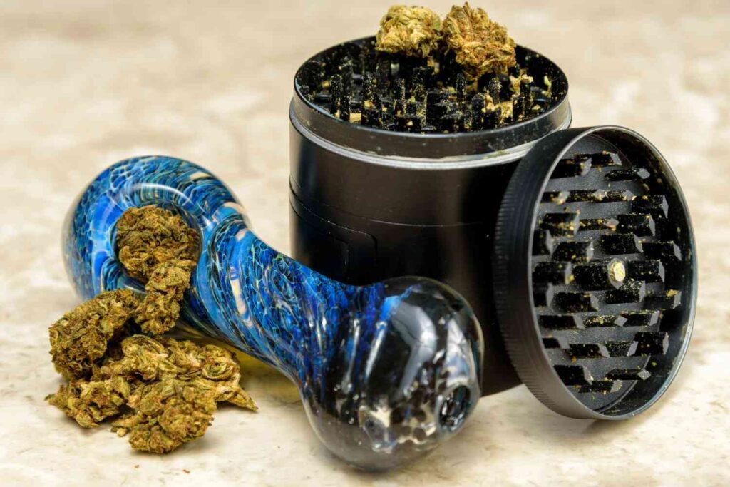 Premium glass pipes Tulsa selection featuring a blue swirl spoon pipe alongside cannabis buds and a black grinder.