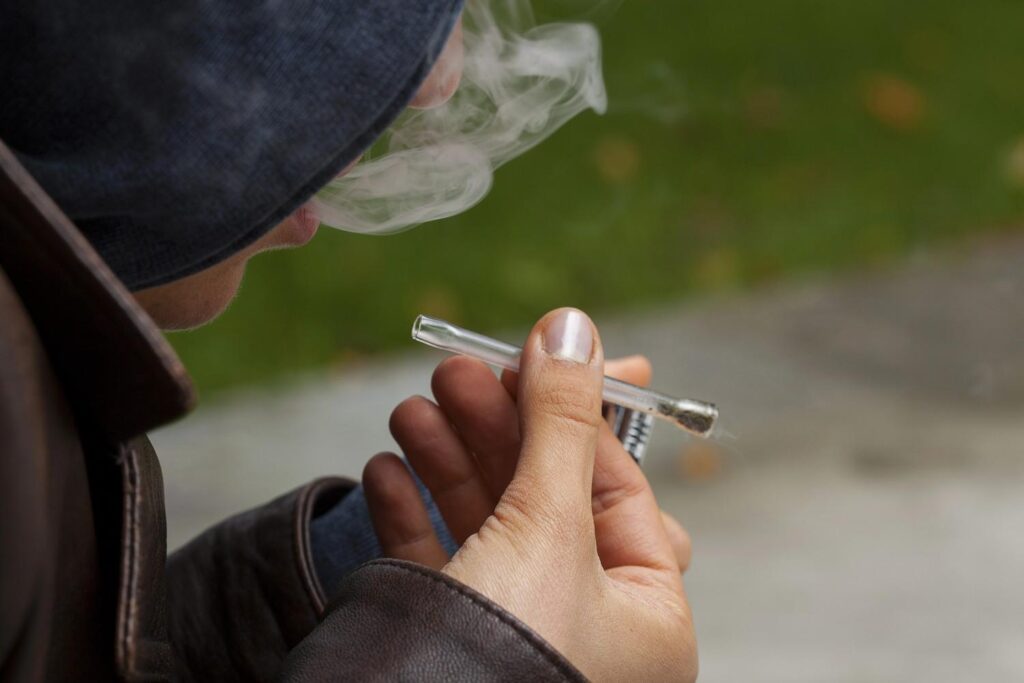 Person using discreet clear glass pipes Tulsa one hitter style chillum outdoors while exhaling a cloud of dense smoke 