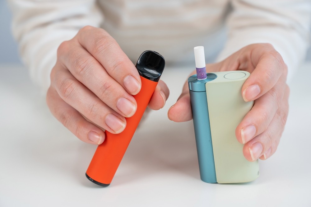 Hands compare an orange pod vape to a modern heat-not-burn device, showcasing sleek product options from a top smoke store broken arrow.