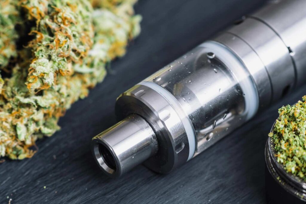 Close up of metallic vape tank hardware near cannabis flower, showcasing quality herbal vaporizers tulsa. 
