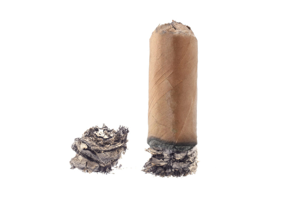 Isolated photo of a short, lit cigar stub resting on ash with more ash next to it, from our Cigar store sapulpa.