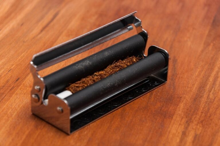 Metal rolling machine preparing loose tobacco and filter tip on a wooden desk. Best rolling papers sapulpa guide.