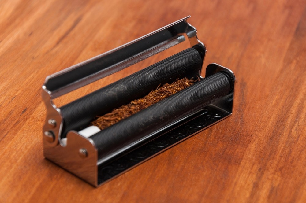 Metal rolling machine preparing loose tobacco and filter tip on a wooden desk. Best rolling papers sapulpa guide.