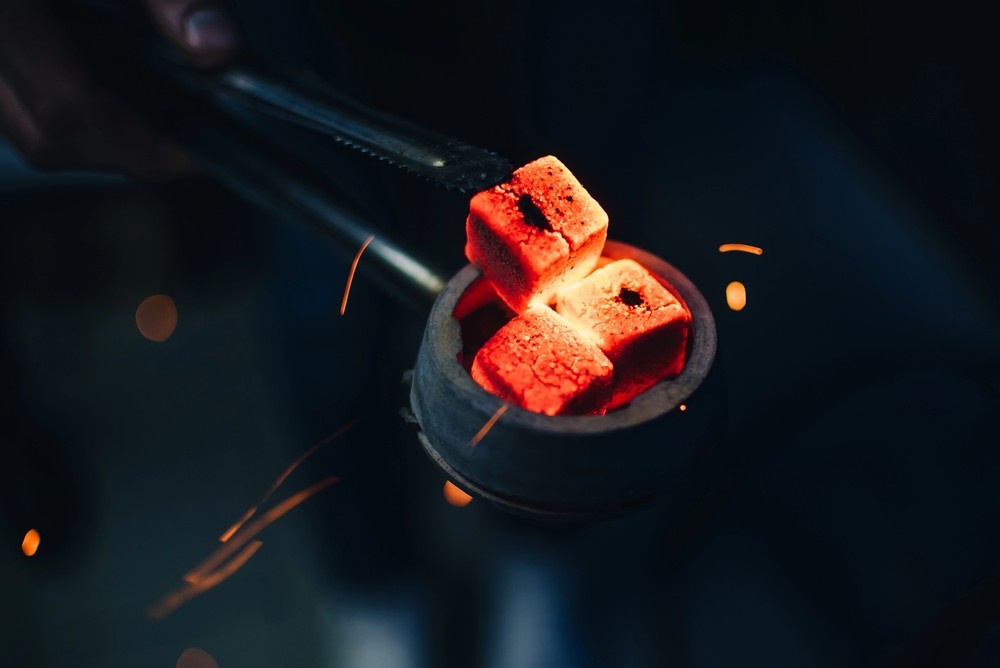 Metal tongs placing glowing red hookah charcoal cubes onto a burner bowl, ready for smoking at our hookah shop houston.