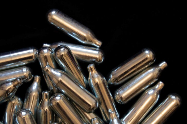 Scattered small steel cylinders on a dark surface, highlighting n20 Broken Arrow cream charger kitchen products.
