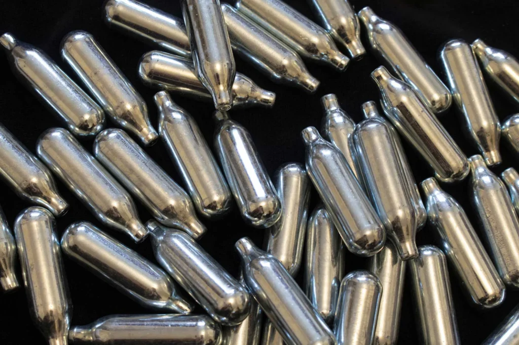 Pile of silver whipped cream chargers on black background, showcasing n20 Broken Arrow culinary supplies. 