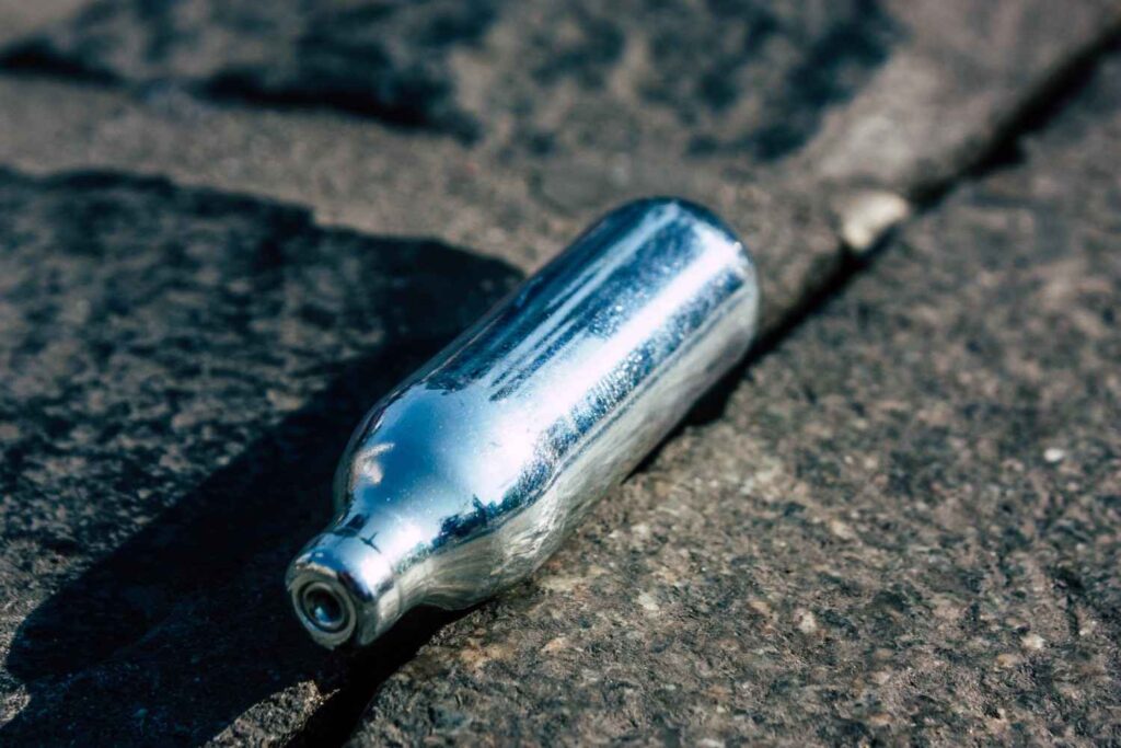 A single metal cartridge and small nitrous oxide whippit charger resting outdoors on concrete for n20 Sapulpa. 