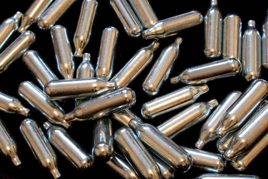 Scattered n2O Owasso whipped cream chargers and stainless steel canisters lying on a dark surface.