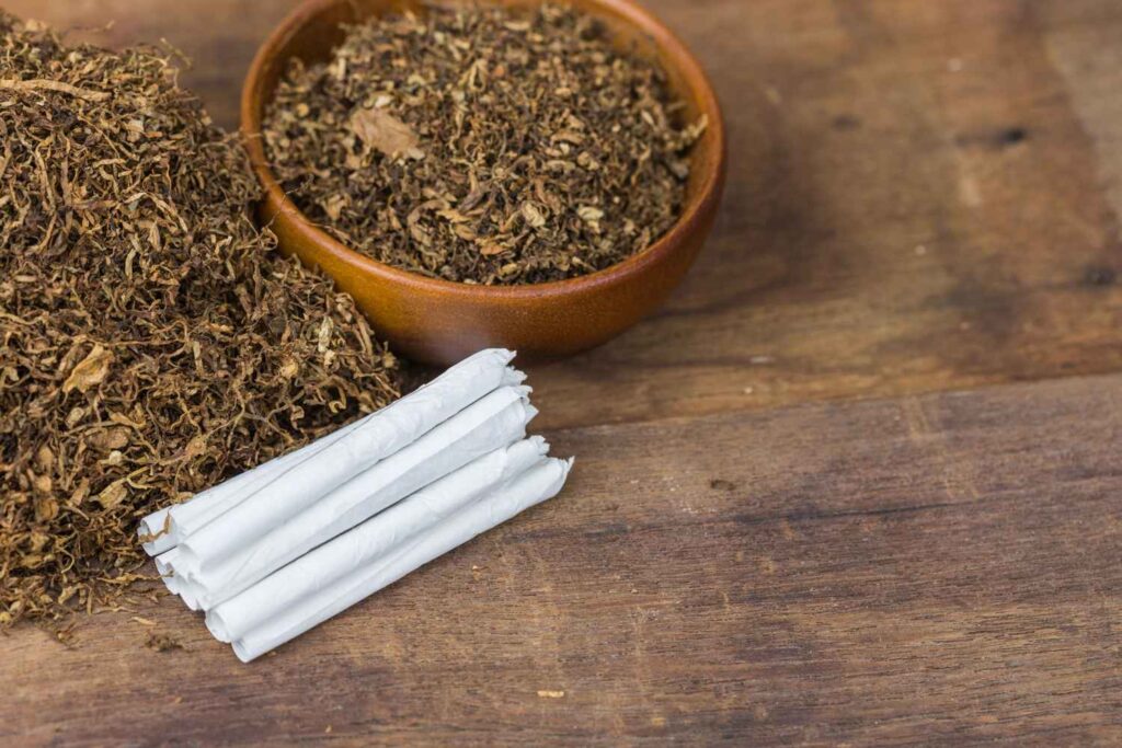 Premium loose leaf tobacco in a wooden bowl with hand-rolled cigarettes from a top tobacco store Tulsa retailer.