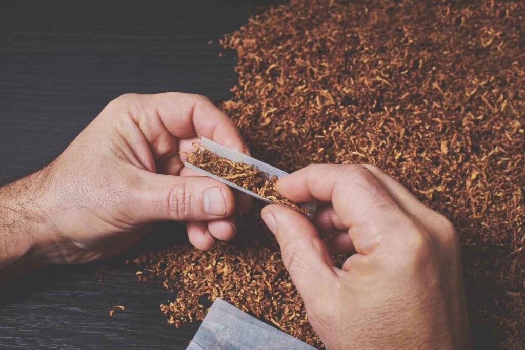 Rolling loose leaf blend from a tobacco shop Houston with rolling paper over a dark wooden table background. 