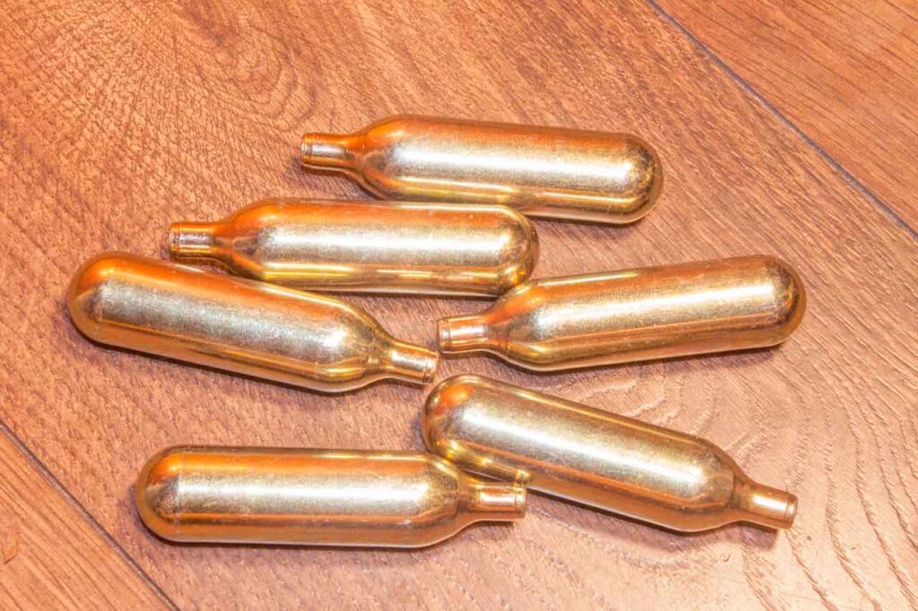 Gold nitrous oxide cartridges displayed on wood floor from a premium smoke shop Tulsa distributor.